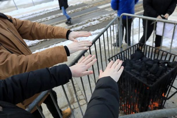 Ludzie grzejący się przy koksowniku stojącym na chodniku